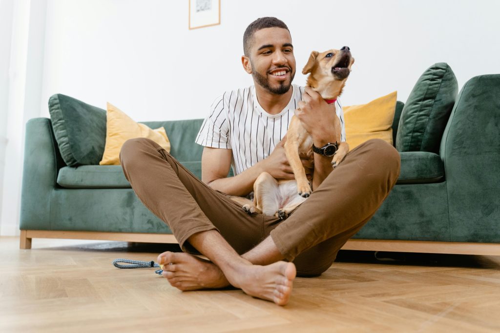Smiling man sitting on floor, playing with his cute pet dog in a cozy living room setting.